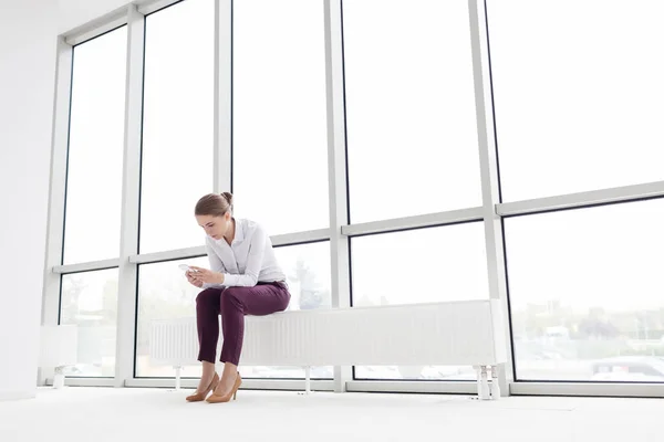 Jonge Zakenvrouw Met Smartphone Tijdens Het Zitten Radiator Nieuw Leeg — Stockfoto