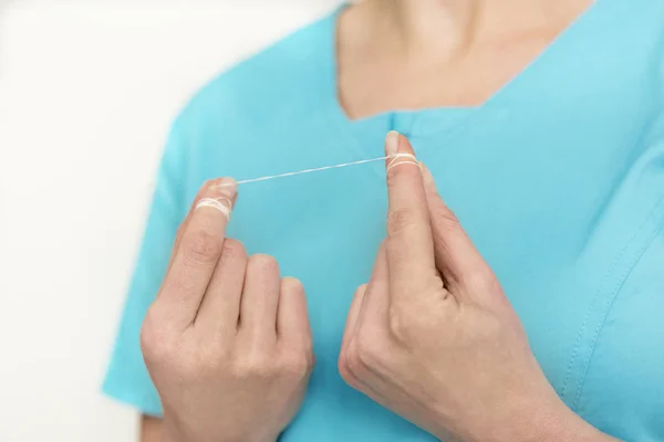 Midsection of dentist in scrubs holding dental floss at clinic