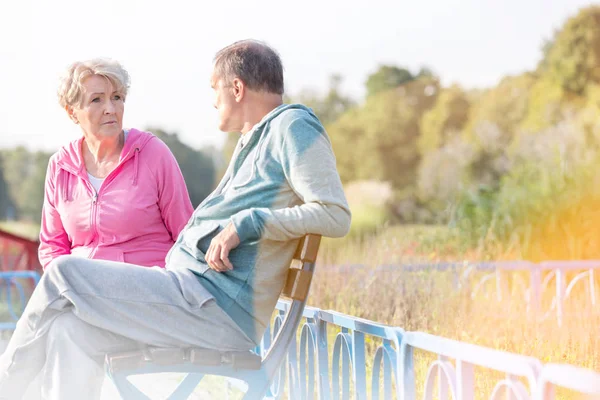 Active senior couple talking while resting on bench at park