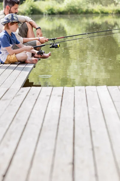 父亲和儿子坐在码头上 在湖里钓鱼 — 图库照片