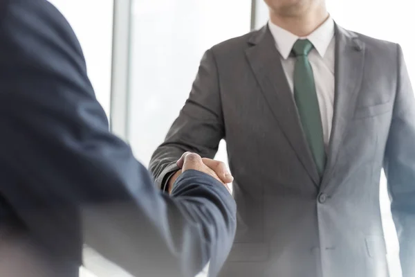 オフィスでの会議中に役員室に立っている間に握手をするビジネスマンの中間部 — ストック写真