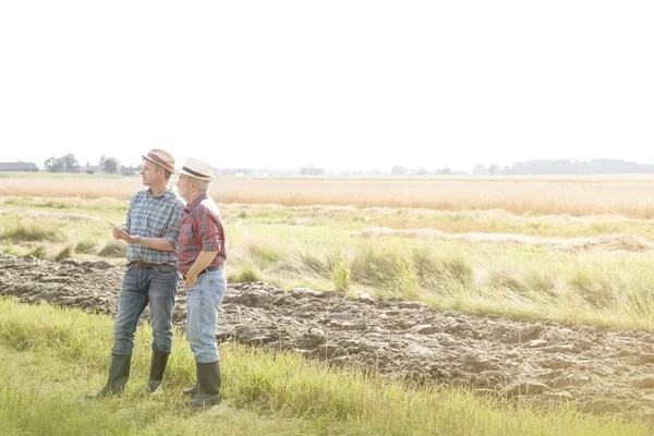 Farmers discussing over digital tablet on field against sky at farm