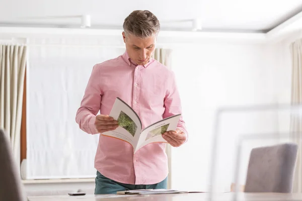 Älterer Mann Liest Broschüre Während Wohnung Tisch Steht — Stockfoto