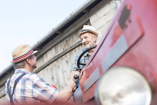 成熟した男農家の納屋に対してトラクターの上に座っての握手 — ストック写真