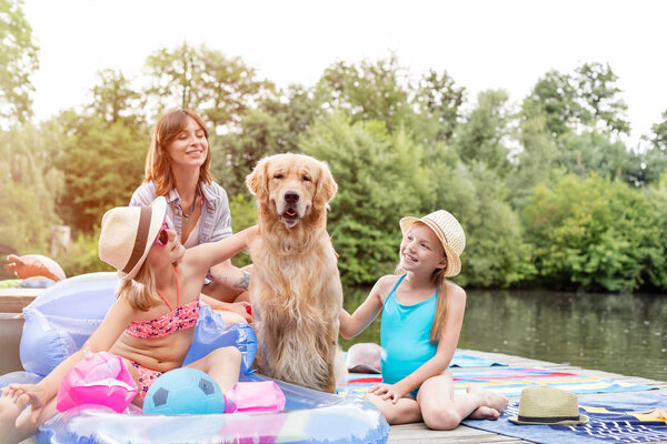 Golden retriever sitting amidst girls and woman on pier against trees