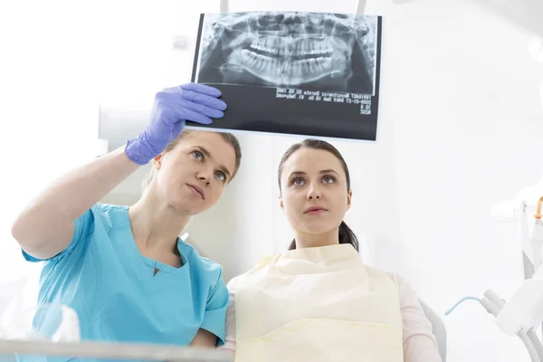 Female dentist showing x-ray to woman at dental clinic