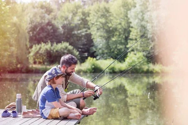 全程的父亲协助儿子在湖里钓鱼 而坐在码头 — 图库照片