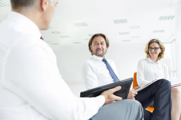 Smiling colleagues looking at businessman while sitting in new office during meeting