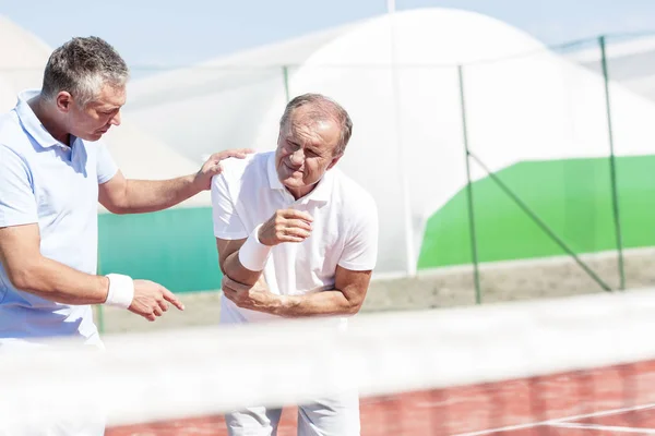 Зрелый Мужчина Помогает Старшему Другу Травмой Локтя Время Игры Теннис — стоковое фото
