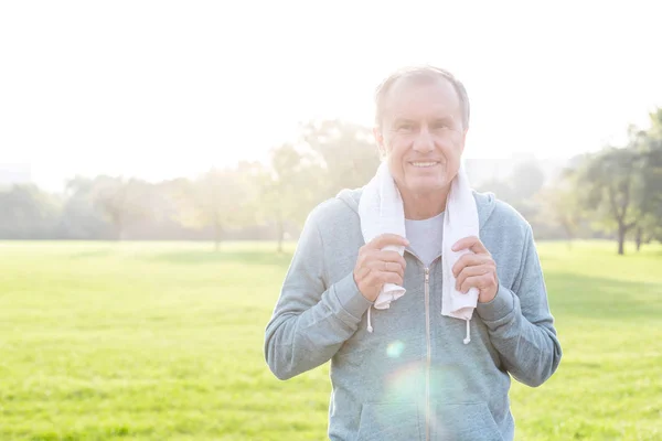 Senior man in sportswear holding towel in park on sunny day