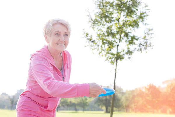 Healthy senior woman throwing disc in park