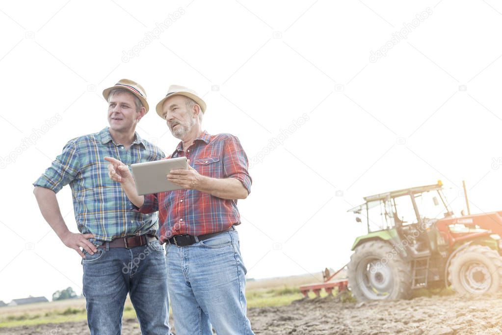 Farmers with digital tablet discussing on field against sky at farm
