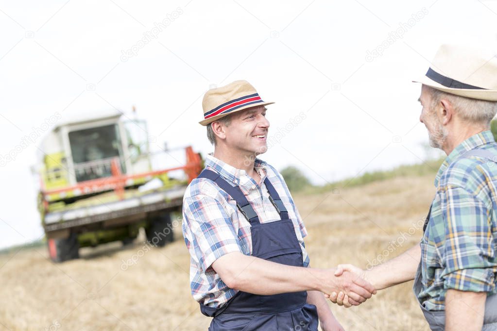 Farmers shaking hands while standing on field at farm