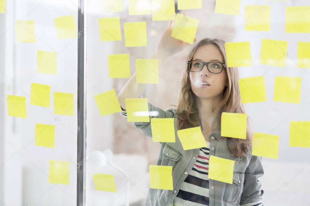 Businesswoman analyzing adhesive notes stuck on glass wall
