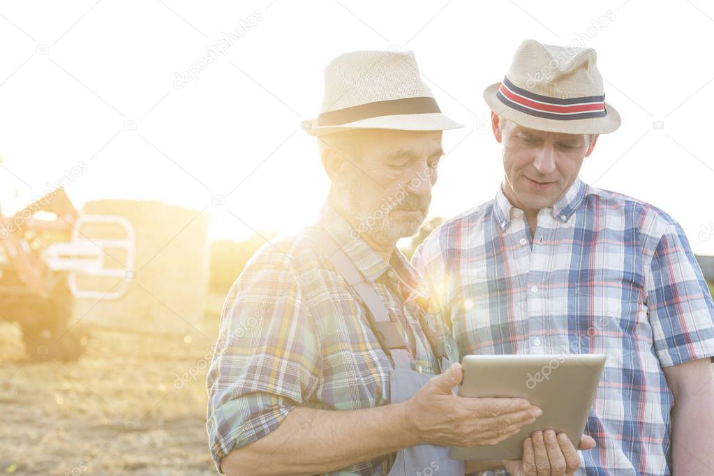 Farmers using digital tablet against sky at farm on sunny day