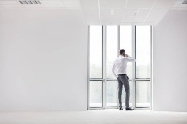 Yeni ofiste akıllı telefonda konuşan genç işadamının tam uzunlukta arka görünümü