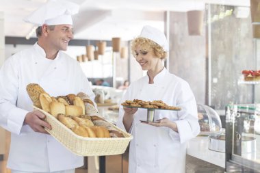 Restoranda taze pişmiş ekmek ve kurabiye tutan gülümseyen olgun şef iş arkadaşları