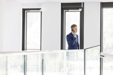 Genç işadamı korkuluk ofis tarafından duran smartphone cep telefonu ile konuşmak