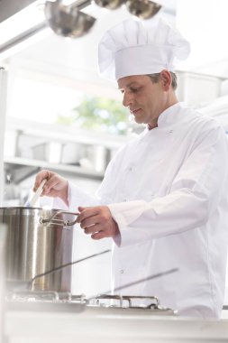 Kendine güvenen chef restoranda mutfakta ocakta çelik tencerede pişirme