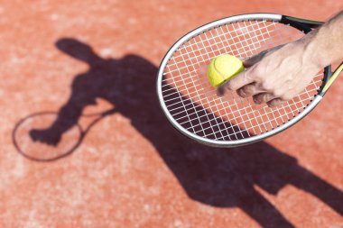 Olgun adam tenis topu kırmızı sahasında güneşli gün boyunca hizmet veren eli kırpılmış