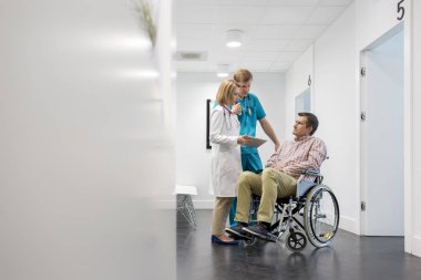 Hastanede tekerlekli sandalyedeki hastayı açıklayan dijital tabletli olgun doktor