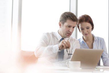 İş arkadaşları ofiste yönetim kurulu odasında otururken dizüstü bilgisayar üzerinde tartışıyor