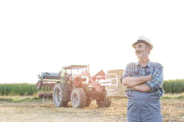 微笑的农夫站立与胳膊横渡对收割者在农场 — 图库照片