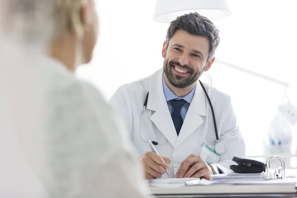 Médico Sorridente Discutindo Com Paciente Maduro Enquanto Escrevia Prescrição Mesa — Fotografia de Stock