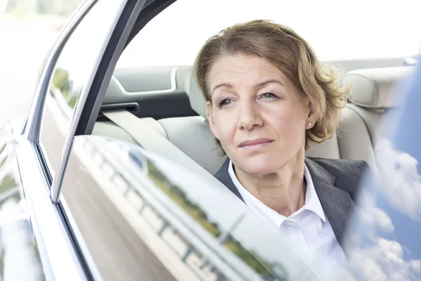 坐在车里的有思想的女商人透过窗户往外看 — 图库照片