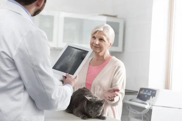 獣医クリニックでデジタルタブレットで立っている医師を見ているシニア女性 — ストック写真