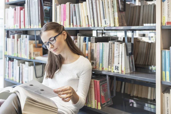Vrouw Boek Lezen Terwijl Zit Tegen Boekenplank Bij Bibliotheek — Stockfoto