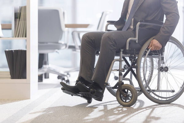 Низкий угол обзора бизнесмена-инвалида на инвалидной коляске в современном офисе
