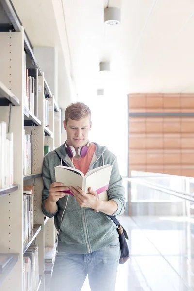 大学图书馆的年轻男生书架上阅读书籍 — 图库照片