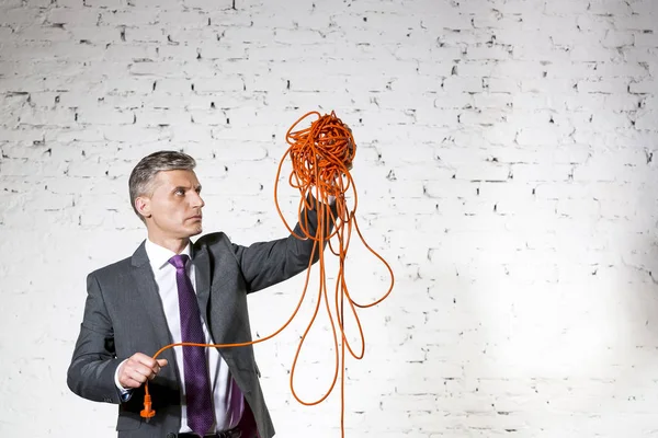 Zelfverzekerde Volwassen Zakenman Houdt Verwarde Kabel Tegen Witte Bakstenen Muur — Stockfoto