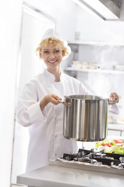 在餐厅的厨房里 微笑的厨师拿着钢锅在炉子上的肖像 — 图库照片