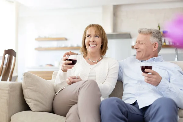 Usmívající Starší Pár Sedí Pohovce Zatímco Drží Drinky Doma — Stock fotografie