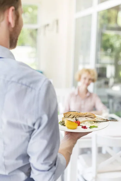 レストランのテーブルに座っている成熟した顧客に昼食を提供するウェイター — ストック写真
