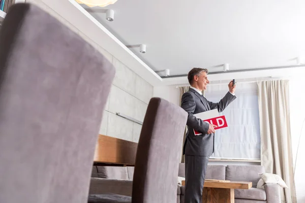 Confident Mature Male Realtor Holding Sold Placard While Photographing Home — Stock Photo, Image
