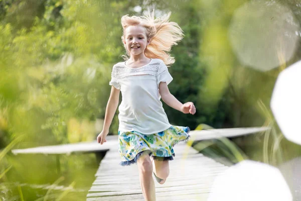 微笑的金发女孩在湖岸的码头上奔跑 — 图库照片