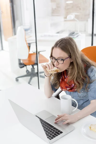 在办公室吃早餐时使用笔记本电脑触摸板的女商人 — 图库照片