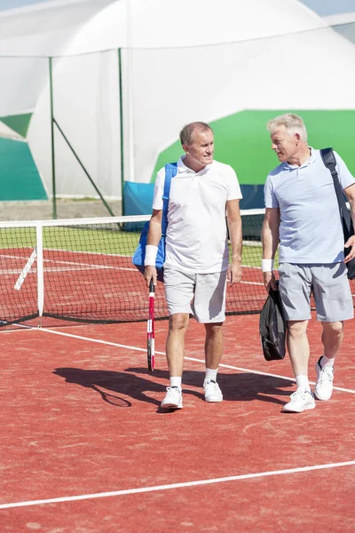 夏の週末の間にテニスコートで歩きながら話しているスポーツウェアの男性の完全な長さ — ストック写真