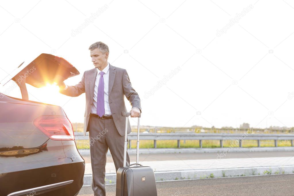 Business executive removing suitcase from car trunk on road against sky