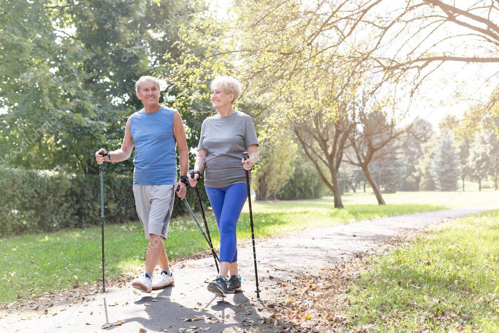 Happy senior couple with hiking poles walking in park