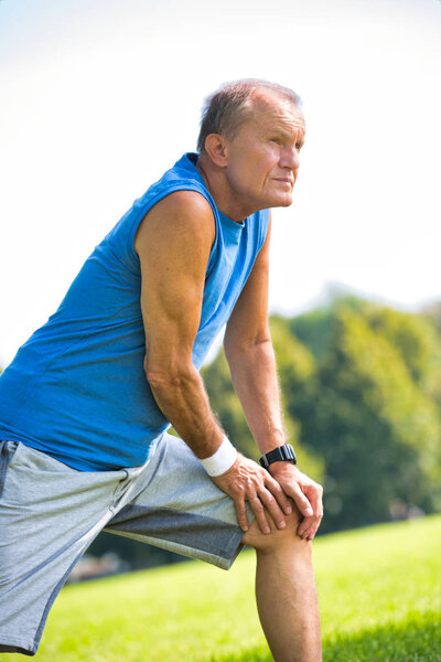 Active senior man stretching leg in park on sunny day