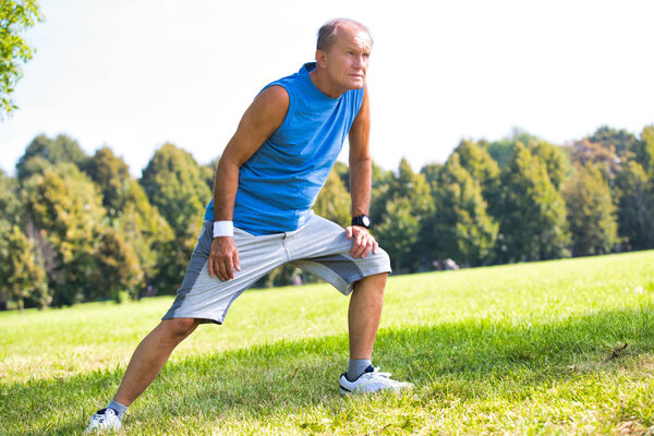 Active senior man stretching leg in park on sunny day