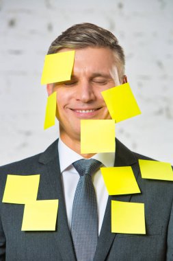 Ofiste yüz ve takım elbise boş sarı yapıştırıcı notları ile gülümseyen olgun işadamı portresi