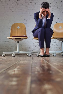 Ofis lobisinde beyaz tuğla duvara karşı oturan baş ağrısı ile genç iş kadını