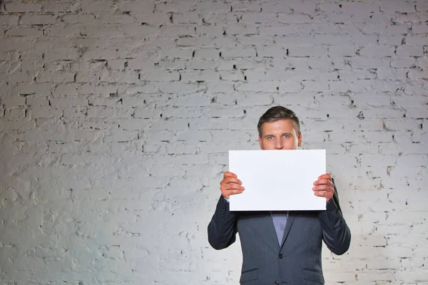 Midsection of businessman holding blank placard while standing against white brick wall