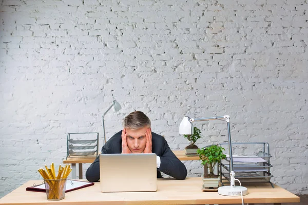オフィスの机の上でラップトップを見て働き過ぎの成熟したビジネスマン — ストック写真