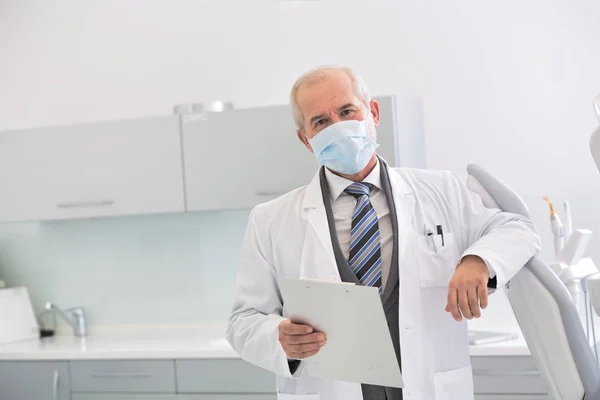 Retrato de dentista sênior usando máscara na clínica odontológica — Fotografia de Stock